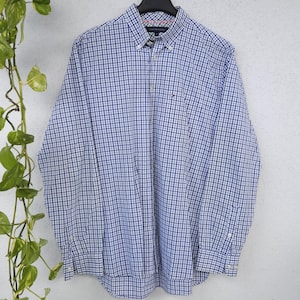 Könnte beinhalten: Ein langärmeliges Hemd mit Knopfleiste und blau-weißem Karomuster. Das Hemd hat einen Button-Down-Kragen, eine durchgehende Knopfleiste vorne und ein kleines gesticktes Logo auf der linken Brust. Die Manschetten sind mit Knöpfen verstellbar.