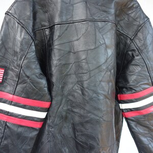 K&ouml;nnte beinhalten: Schwarze Lederjacke mit roten und wei&szlig;en Streifen an den &Auml;rmeln und einem kleinen amerikanischen Flaggen-Patch auf der linken Brust. Die Jacke ist aus Patchwork-Leder mit einem einzigartigen Design.