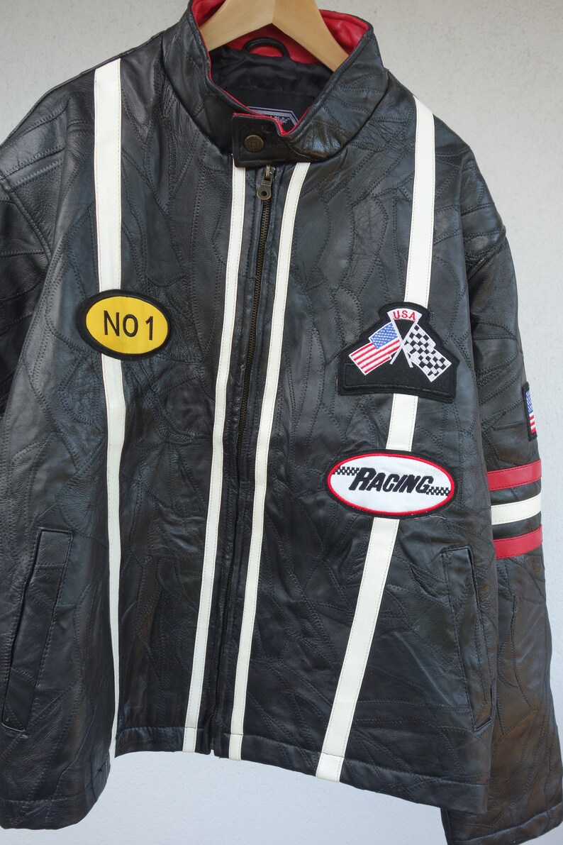 K&ouml;nnte beinhalten: Schwarze Leder-Rennjacke mit wei&szlig;en Streifen und roten Akzenten. Sie hat Patches mit dem Text "NO 1", "USA" und "RACING".