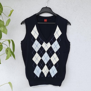 Può includere: Un maglione blu navy senza maniche con un motivo a rombi bianchi e blu chiaro. Il maglione ha un collo a V e un'etichetta rossa sul retro.