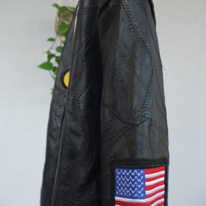 K&ouml;nnte beinhalten: Schwarze Lederjacke mit gestepptem Design und einem roten und wei&szlig;en amerikanischen Flaggen-Patch am &Auml;rmel.
