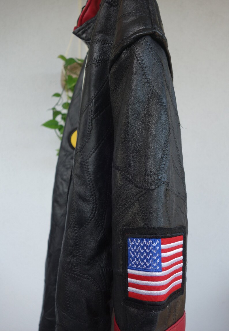 K&ouml;nnte beinhalten: Schwarze Lederjacke mit gestepptem Design und einem roten und wei&szlig;en amerikanischen Flaggen-Patch am &Auml;rmel.