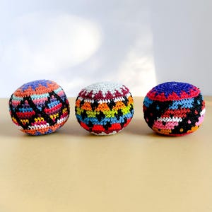 Puede incluir: Tres bolas de ganchillo coloridas con patrones geométricos. Las bolas presentan una variedad de colores, incluyendo negro, naranja, azul, rosa y blanco. Las bolas son redondas y parecen hechas a mano, ideales para malabares o decoración.