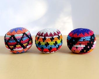 以下が含まれることがあります： 幾何学模様のカラフルな手編みボールが3つ。黒、オレンジ、青、ピンク、白など様々な色を使用。これらの丸いボールは手作りで、ジャグリングや装飾に最適です。