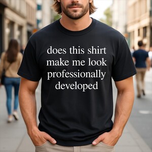 Könnte beinhalten: Ein schwarzes kurzärmeliges T-Shirt mit Rundhalsausschnitt und weißem Text auf der Brust, der lautet, does this shirt make me look professionally developed. Das Kleidungsstück hat eine Standardpassform mit geripptem Ausschnitt und schwarzem Stoff.