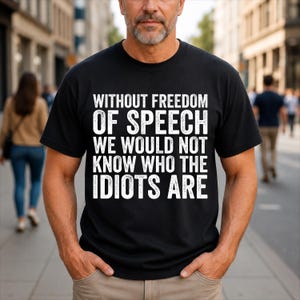 May include: A black short-sleeved t-shirt featuring white text that reads: WITHOUT FREEDOM OF SPEECH WE WOULD NOT KNOW WHO THE IDIOTS ARE. The shirt has a crew neckline and a standard fit, displaying the bold, capitalized lettering across the chest.