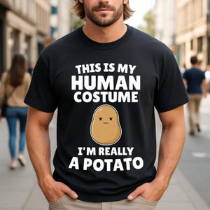 Könnte beinhalten: Schwarzes T-Shirt mit dem Text "THIS IS MY HUMAN COSTUME" über einer Cartoon-Kartoffel-Illustration und dem Text "I'M REALLY A POTATO". Das T-Shirt wird von einer Person getragen.