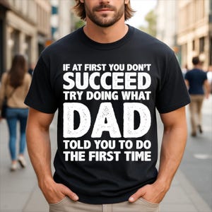 May include: A black short-sleeved t-shirt featuring white text that reads: IF AT FIRST YOU DON'T SUCCEED TRY DOING WHAT DAD TOLD YOU TO DO THE FIRST TIME. The lettering is bold and capitalized, centered on the chest of the garment.