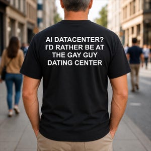 May include: A black short-sleeved t-shirt featuring white text on the back that reads: AI DATACENTER? I'D RATHER BE AT THE GAY GUY DATING CENTER. The shirt has a crew neckline and is worn with light brown trousers, viewed from the back.