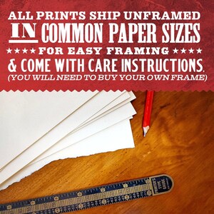 a wooden table with a stack of white paper sheets, a red pencil, and a ruler, along with text that reads "All prints ship unframed in common paper sizes for easy framing & come with care instructions. (You will need to buy your own frame)"