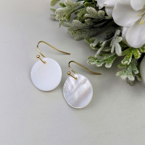 May include: A pair of white mother of pearl earrings with gold hooks. The earrings are round and have a smooth, polished finish.