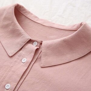 K&ouml;nnte beinhalten: Nahaufnahme eines rosa Hemdes mit Kn&ouml;pfen, einem wei&szlig;en Kragen und wei&szlig;en Kn&ouml;pfen.