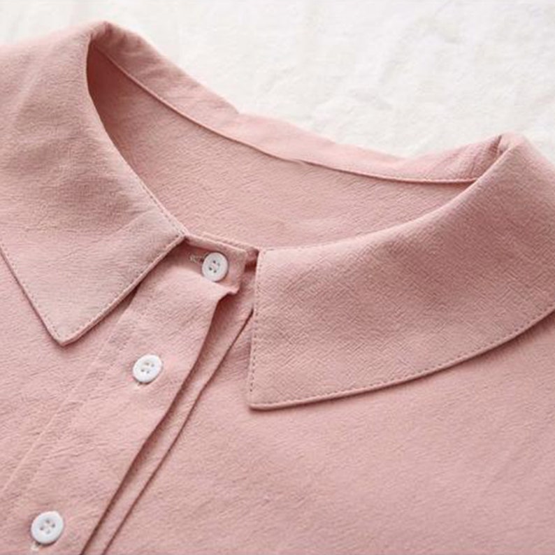 K&ouml;nnte beinhalten: Nahaufnahme eines rosa Hemdes mit Kn&ouml;pfen, einem wei&szlig;en Kragen und wei&szlig;en Kn&ouml;pfen.