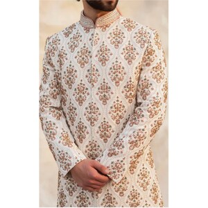 May include: A white long-sleeved garment with a mandarin collar and intricate floral embroidery in shades of pink, green, and gold.