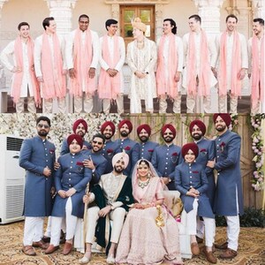 May include: A wedding ceremony with a bride and groom in traditional Indian attire. The groom is wearing a white sherwani with a green shawl, and the bride is wearing a pink lehenga with a red dupatta. The groom's friends are wearing blue sherwanis with white turbans. The bride's friends are wearing pink dupattas.