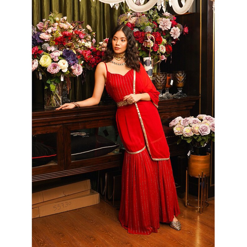 Puede incluir: Un vestido rojo a rayas de largo hasta el suelo con un cintur&oacute;n dorado y un dupatta rojo a juego. El vestido tiene una falda de capas y est&aacute; adornado con adornos dorados.