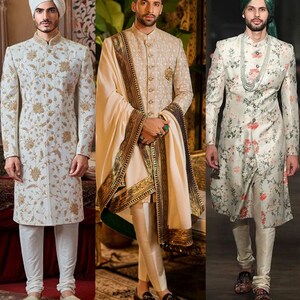 Op de afbeelding: Drie mannen in traditionele Indiase trouwjurken. De mannen dragen witte kurta's met bloemenborduurwerk, witte broeken en tulbanden. De kurta's zijn versierd met gouden borduurwerk. De mannen staan voor een achtergrond met een patroon.