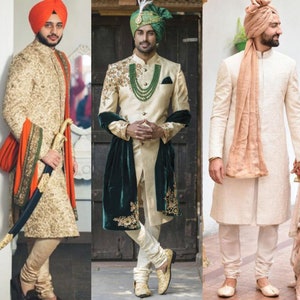 Op de afbeelding: Drie mannen in traditionele Indiase trouwkledij. De mannen dragen gouden en witte sherwanis met uitgebreide borduurwerk. Ze dragen ook turbans in verschillende kleuren en stijlen.