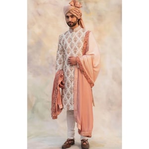 May include: A white and pink patterned men's outfit with a pink turban. The outfit includes a long-sleeved shirt, pants, and a shawl.