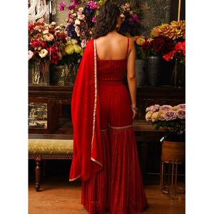 Puede incluir: Un mono rojo sin mangas, largo hasta el suelo, con la parte inferior acampanada y ribetes dorados. El mono tiene un corpi&ntilde;o ajustado y una dupatta ancha y fluida.