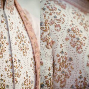 May include: White fabric with intricate floral embroidery in shades of pink, gold, and blue. The embroidery features delicate floral patterns and swirls.
