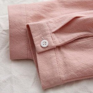 K&ouml;nnte beinhalten: Nahaufnahme eines rosa lang&auml;rmeligen Hemdes mit einem wei&szlig;en Knopf am &Auml;rmel.