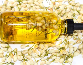 May include: A clear glass bottle with a dropper filled with a yellow liquid and white jasmine flowers. The bottle is labelled "Jasmine Body Oil" and has text that reads "Hair, Nails & Skin, Hand, Love & Care, Geranium, With, Set Almond Oil, Cold Virgin Olive, Essential Oil".