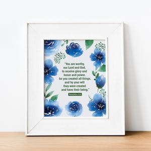 Puede incluir: Una impresión enmarcada con un diseño de acuarela de flores azules y hojas verdes. La impresión presenta un versículo bíblico de Apocalipsis 4:11, que dice: "Tú eres digno, nuestro Señor y nuestro Dios, de recibir la gloria, el honor y el poder. Porque tú creaste todas las cosas, y por tu voluntad fueron creadas y tienen su ser."