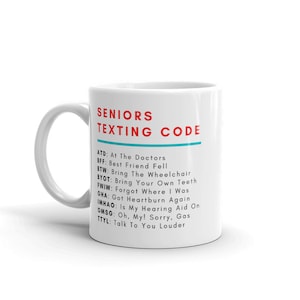 Puede incluir: Taza de cerámica blanca con un contorno negro y texto rojo que dice "Seniors Texting Code". La taza enumera las abreviaturas comunes de mensajes de texto para personas mayores y sus significados.