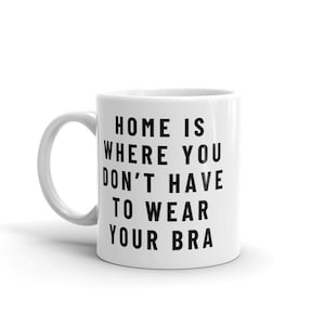 May include: White ceramic coffee mug with black text that reads "Home is where you don't have to wear your bra."