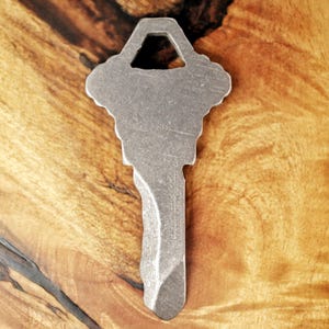 May include: A silver key with a unique design, featuring a hole in the top and a textured surface. The key is made of metal and has a sharp point at the bottom.
