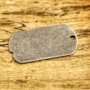 Pode incluir: Uma placa de identificação metálica envelhecida, de forma retangular com cantos arredondados, com um furo e uma superfície texturizada. O texto "TITAN TALON TOOL CO." é visível. Sobre uma superfície de madeira.