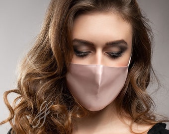 May include: A woman wearing a light pink satin face mask. The mask has a simple design and is made of a soft, comfortable material.