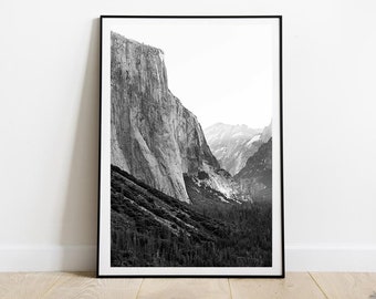 May include: A black and white photograph of a mountain range with a large cliff face in the foreground. The image is taken from a low angle, looking up at the mountain.