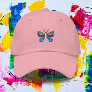 May include: A pink baseball cap with an embroidered butterfly design. The butterfly has blue, yellow, red, and orange wings.