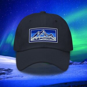 May include: A dark blue baseball cap with an embroidered patch featuring a white mountain range against a blue sky. The patch is surrounded by a white border.