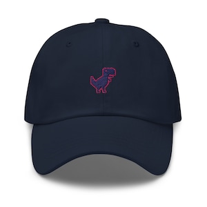 Op de afbeelding: Een donkerblauwe baseballpet met een rood gepixelde dinosaurus geborduurd op de voorkant.