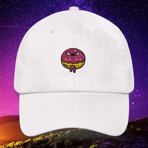 May include: White baseball cap with a pink and yellow donut embroidered on the front. The donut has sprinkles and a dripping glaze.