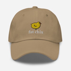 May include: A tan baseball cap with an embroidered yellow chick and the text "fat chix" in white.