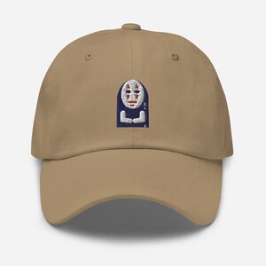 May include: A khaki baseball cap featuring an embroidered image of a white-faced figure with red eyes and a blue robe. The figure is wearing a mask with a red and white design.