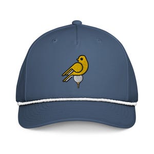 Pode incluir: Boné de beisebol azul marinho com detalhe de corda branca e um pássaro amarelo bordado em uma bola de golfe. O pássaro tem detalhes em preto e branco. O boné tem uma aba curva e um botão na parte superior.