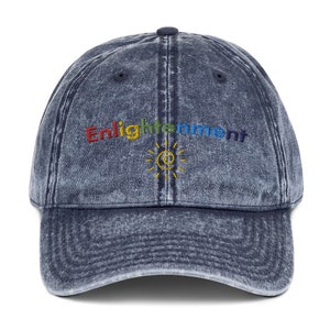 K&ouml;nnte beinhalten: Eine blaue Denim-Baseballkappe mit Used-Look. Die Kappe hat ein regenbogenfarbenes gesticktes Logo mit der Aufschrift "Enlightenment" und einem Sonnensymbol.