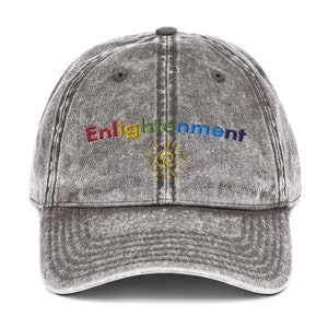 K&ouml;nnte beinhalten: Eine schwarze, abgenutzte Baseballkappe aus Denim mit dem Wort "Enlightenment" in Regenbogenfarben gestickt. Unter dem Wort ist eine gelbe Sonne mit einem stilisierten "C" im Inneren gestickt.