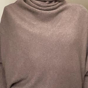 Pu&ograve; includere: Un maglione dolcevita marrone con un design ampio e drappeggiato. Il maglione ha un colletto alto e piegato e una vestibilit&agrave; ampia. Il tessuto sembra essere una maglia morbida, adatta ai climi pi&ugrave; freschi. Le maniche sono lunghe e lo stile generale &egrave; casual.