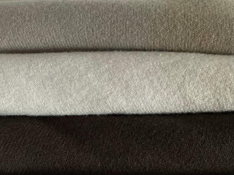 Pu&ograve; includere: Primo piano di tessuto piegato nelle tonalit&agrave; del grigio e del marrone. Lo strato superiore &egrave; grigio chiaro, seguito da un grigio medio, un grigio pi&ugrave; scuro e un marrone scuro in basso. Il tessuto ha una trama a coste.