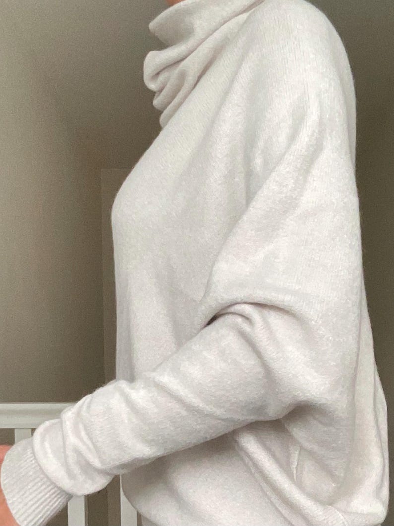 Pu&ograve; includere: Un maglione a collo alto beige chiaro con maniche lunghe. Il maglione ha una vestibilit&agrave; ampia e un polsino a coste al polso. Il tessuto sembra morbido e confortevole.