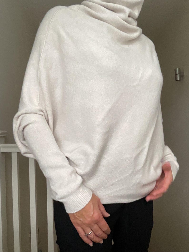 Pu&ograve; includere: Un maglione a collo alto color crema oversize con maniche lunghe. Il maglione ha una vestibilit&agrave; ampia e polsini a coste. La modella indossa pantaloni neri. Il collo alto cade morbidamente, creando un look comodo ed elegante.