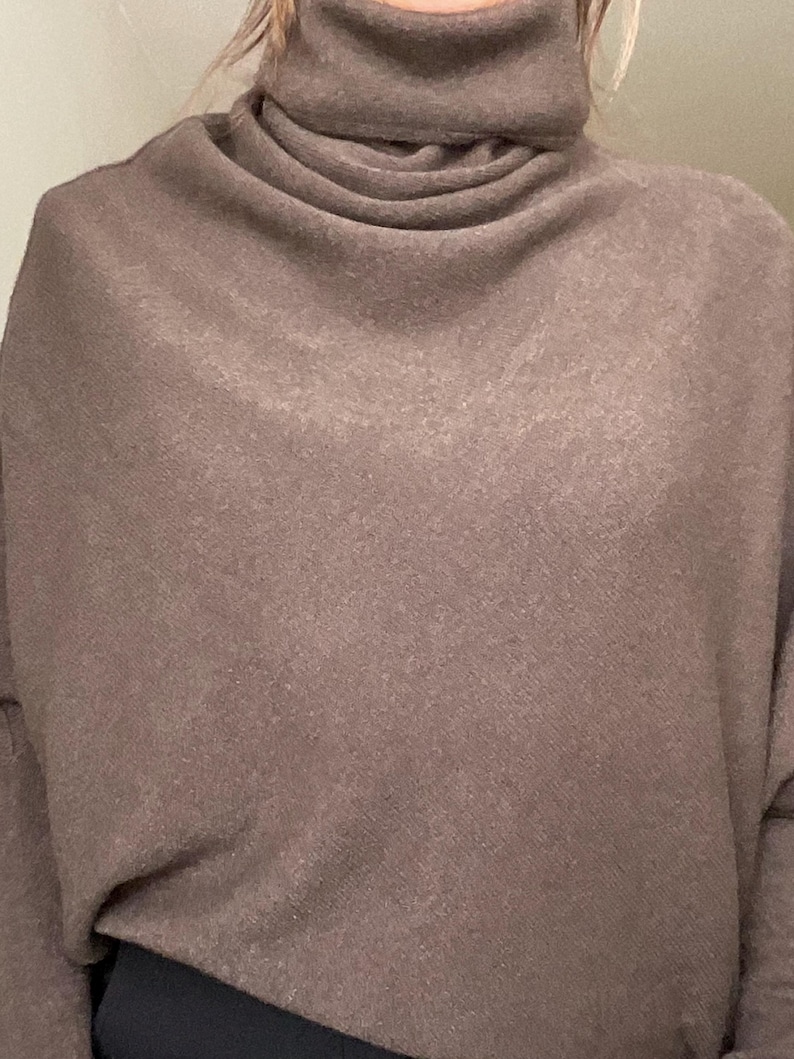 Pu&ograve; includere: Un maglione dolcevita marrone con un design ampio e drappeggiato. Il maglione ha un colletto alto e piegato e una vestibilit&agrave; ampia. Il tessuto sembra essere una maglia morbida, adatta ai climi pi&ugrave; freschi. Le maniche sono lunghe e lo stile generale &egrave; casual.