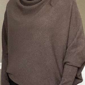 Pu&ograve; includere: Un maglione marrone a collo alto. Il maglione a maniche lunghe ha una vestibilit&agrave; rilassata con uno scollo drappeggiato e un aspetto morbido e strutturato. Le maniche sono lunghe e aderenti ai polsi. Il maglione &egrave; di colore uniforme e sembra essere fatto di un materiale caldo.