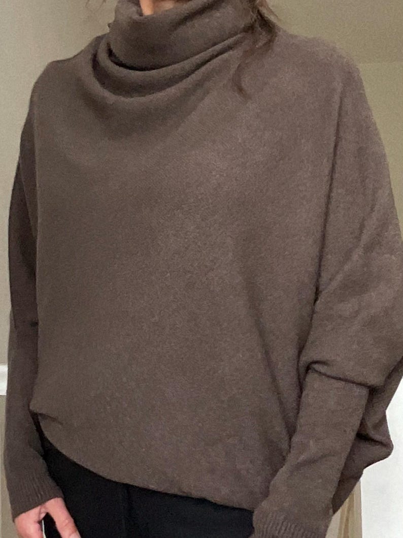 Pu&ograve; includere: Un maglione marrone a collo alto. Il maglione a maniche lunghe ha una vestibilit&agrave; rilassata con uno scollo drappeggiato e un aspetto morbido e strutturato. Le maniche sono lunghe e aderenti ai polsi. Il maglione &egrave; di colore uniforme e sembra essere fatto di un materiale caldo.